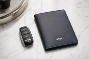 Black Bentley car key fob next to a navy blue leather wallet on a white marble surface.